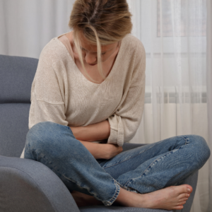Woman sitting cross-legged on a couch holding her stomach in discomfort, illustrating whether a UTI can go away on its own