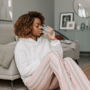 Woman sitting on the floor at home sipping water to support recurrent UTI treatment through increased fluid intake